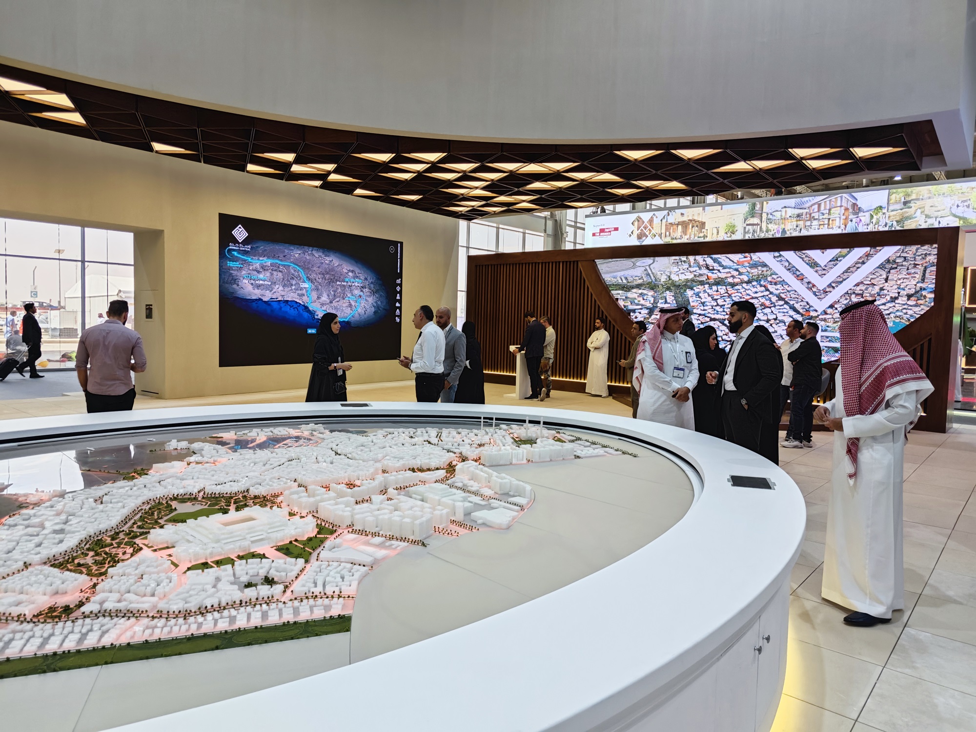 Visitors exploring an immersive digital twin model of Riyadh at an exhibition, displayed on a large curved screen with a scale model in the foreground.