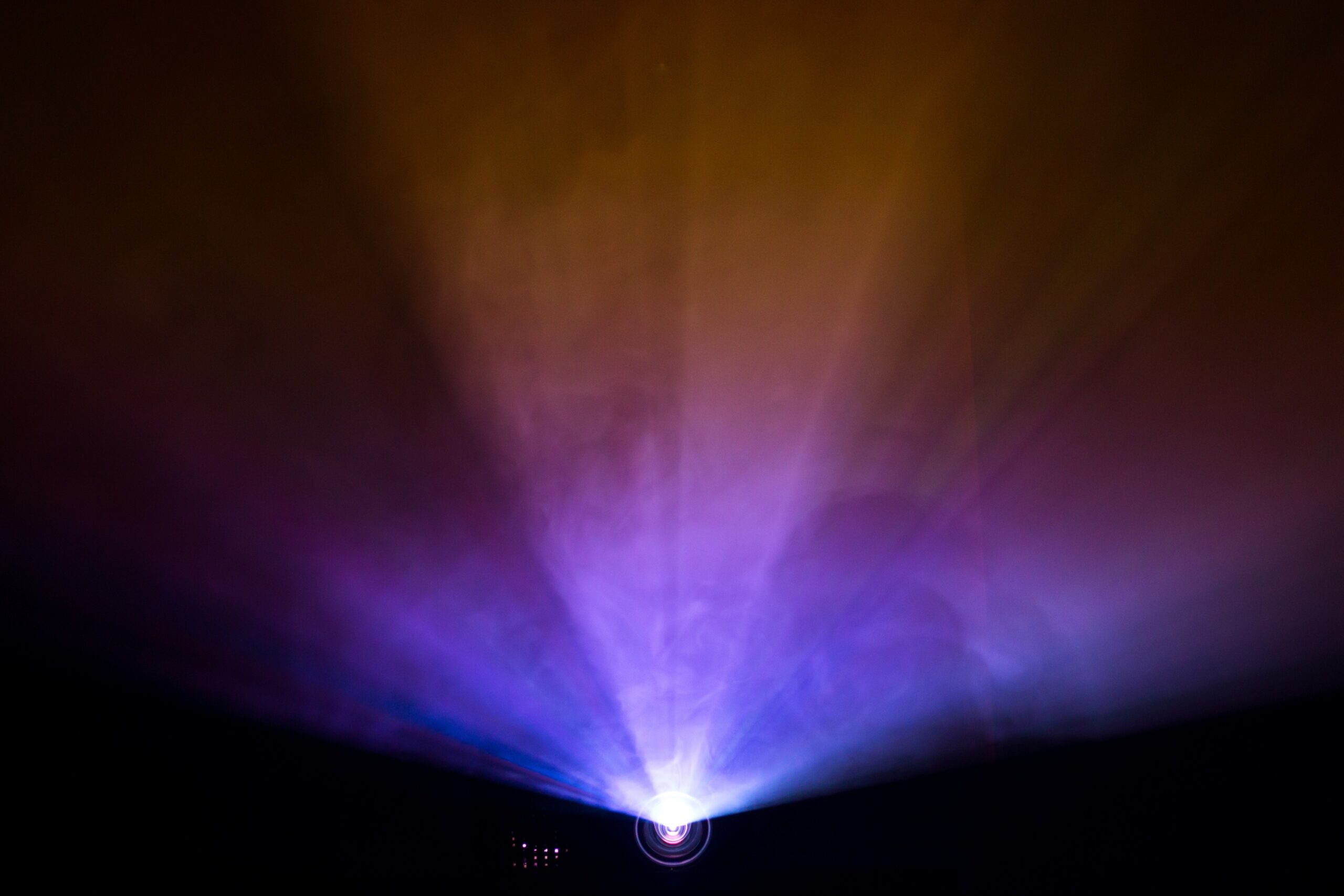 Colorful beams of light from a projector illuminate a dark room, creating a captivating display with shades of purple and gold.