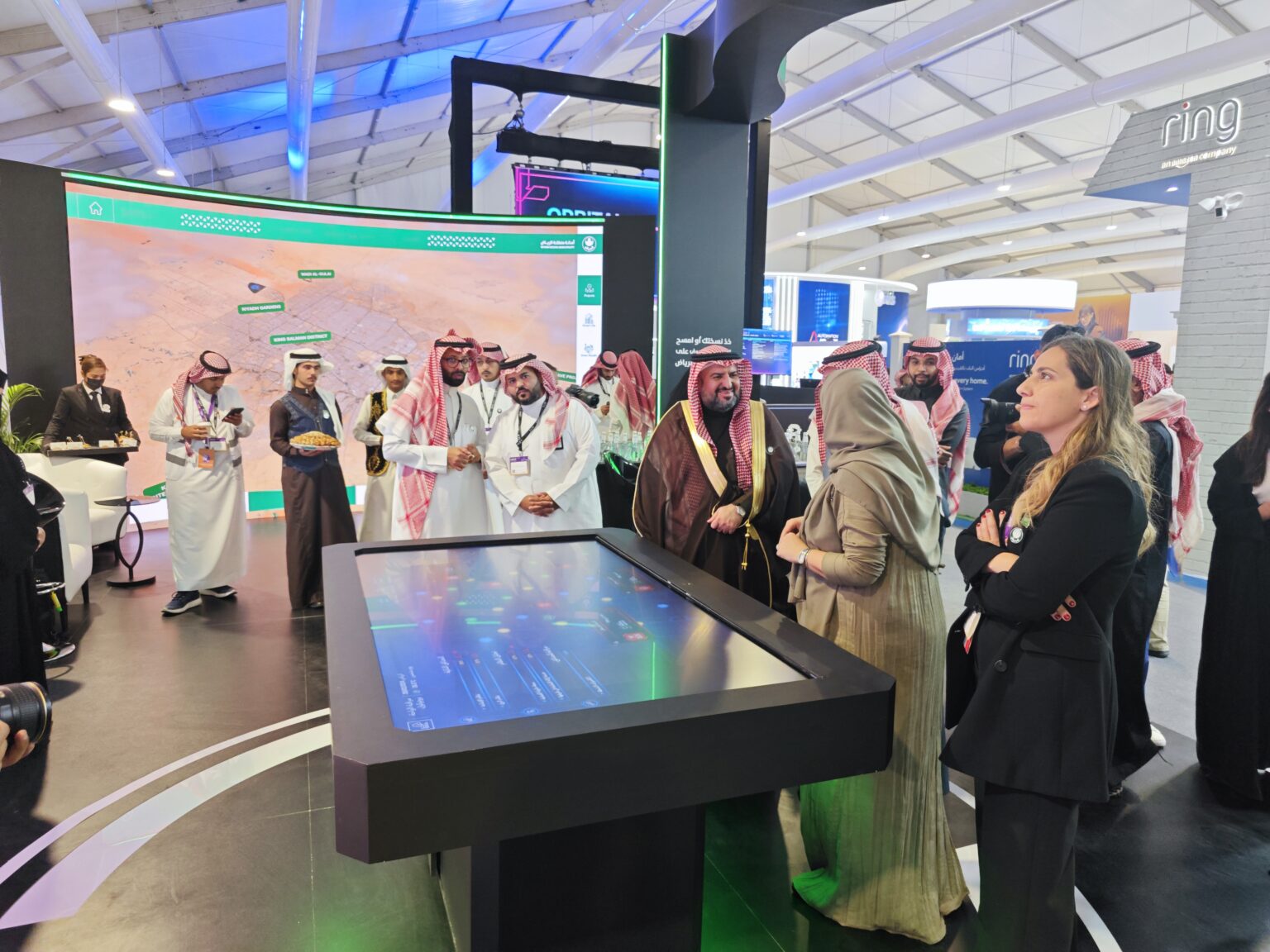 Attendees exploring the Riyadh Digital Twin using a touch table and large exhibition screen.