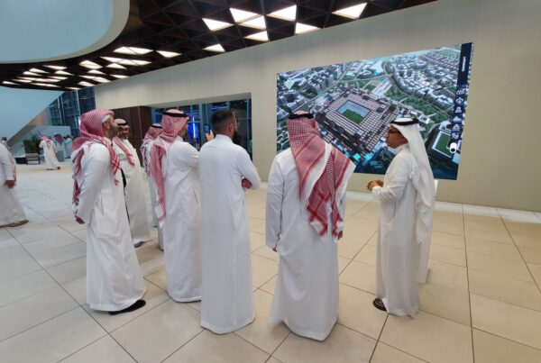 Group of real estate professionals exploring a high-resolution digital twin display of a large-scale urban development project. The interactive and immersive technology, showcased in a trade show setting, demonstrates the power of digital twins and audiovisual solutions for real estate marketing and stakeholder engagement.