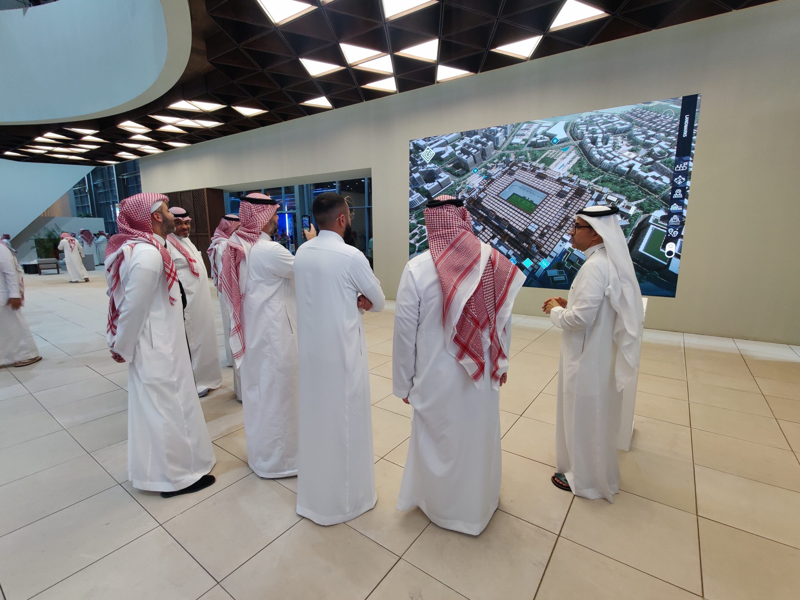 Group of real estate professionals exploring a high-resolution digital twin display of a large-scale urban development project. The interactive and immersive technology, showcased in a trade show setting, demonstrates the power of digital twins and audiovisual solutions for real estate marketing and stakeholder engagement.