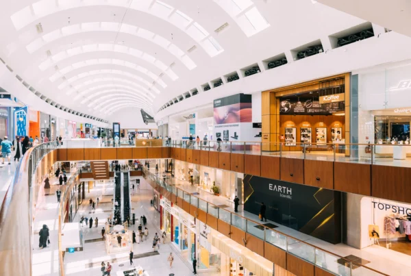 A modern shopping mall featuring smart digital signage displays integrated into the storefronts and open spaces. The digital screens showcase advertisements, promotions, and branding, enhancing customer experience and engagement through visually dynamic content. The architecture includes large open walkways and natural light, highlighting the seamless integration of digital signage in a retail environment.