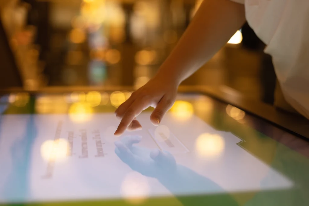 A close-up of a hand interacting with a touchscreen interface, highlighting the use of technology in creating immersive event experiences. The blurred background with warm lighting emphasizes the interactive and engaging atmosphere often associated with modern event setups.
