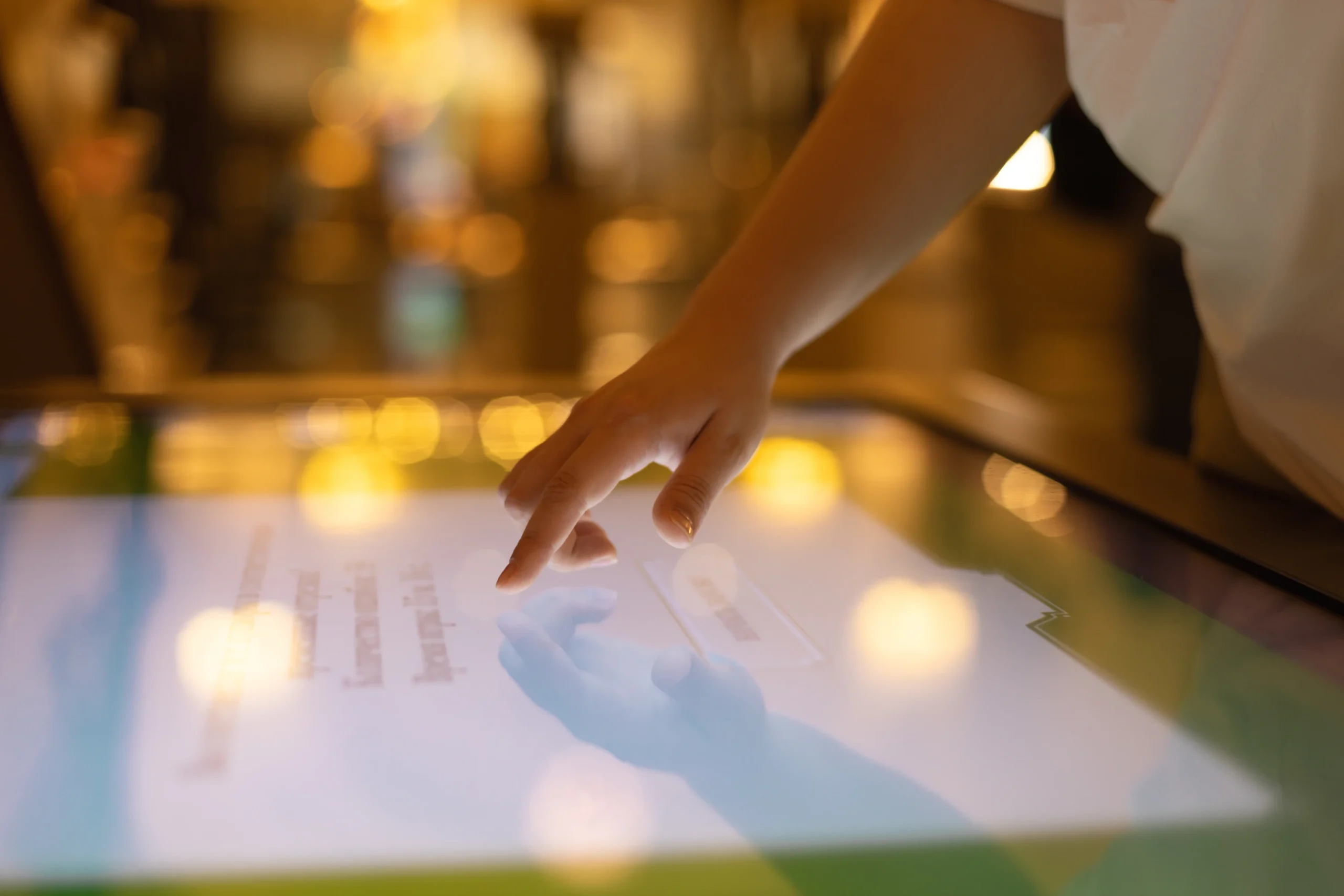 A close-up of a hand interacting with a touchscreen interface, highlighting the use of technology in creating immersive event experiences. The blurred background with warm lighting emphasizes the interactive and engaging atmosphere often associated with modern event setups.