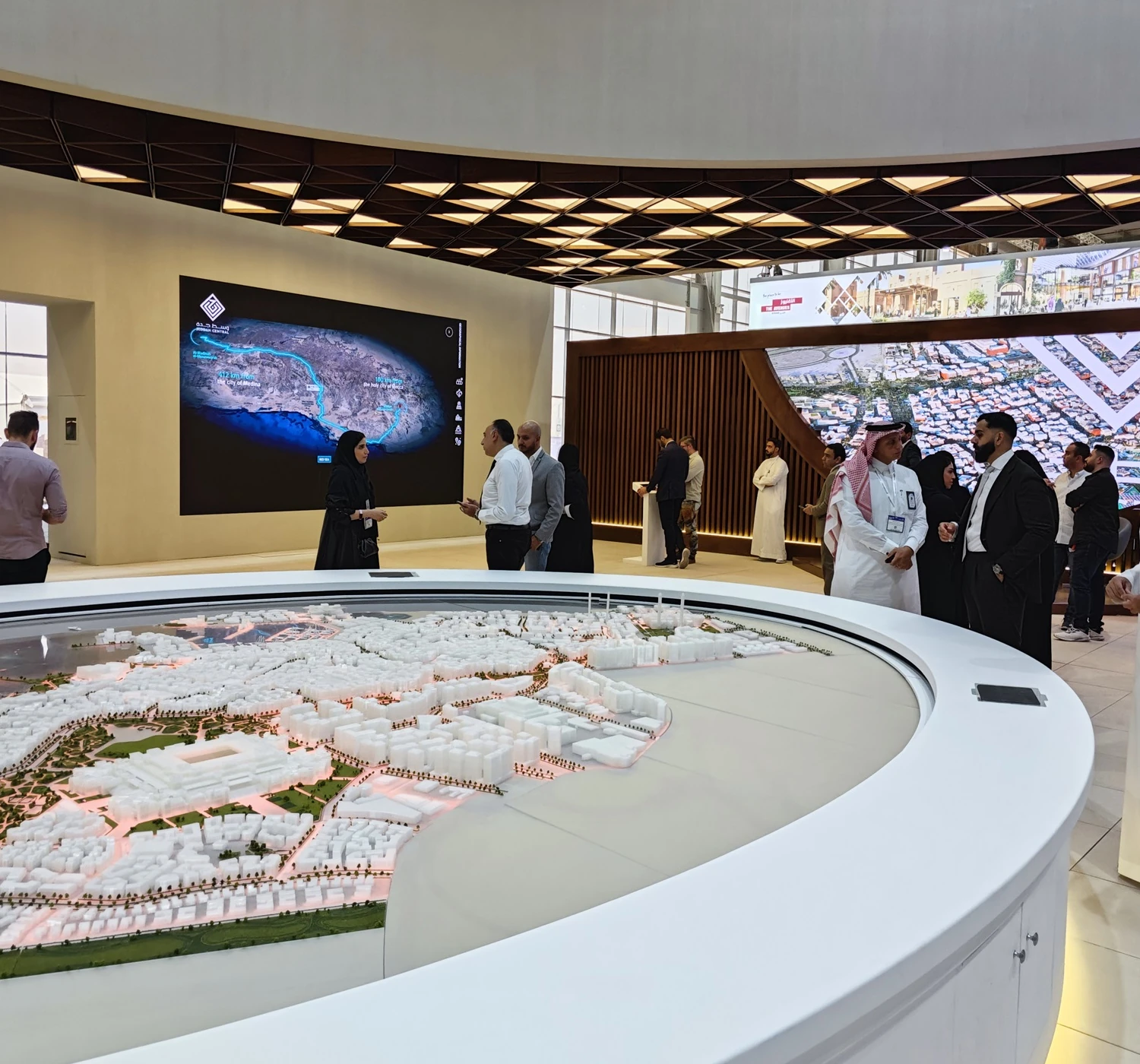 Visitors exploring an immersive digital twin model of Riyadh at an exhibition, displayed on a large curved screen with a scale model in the foreground.