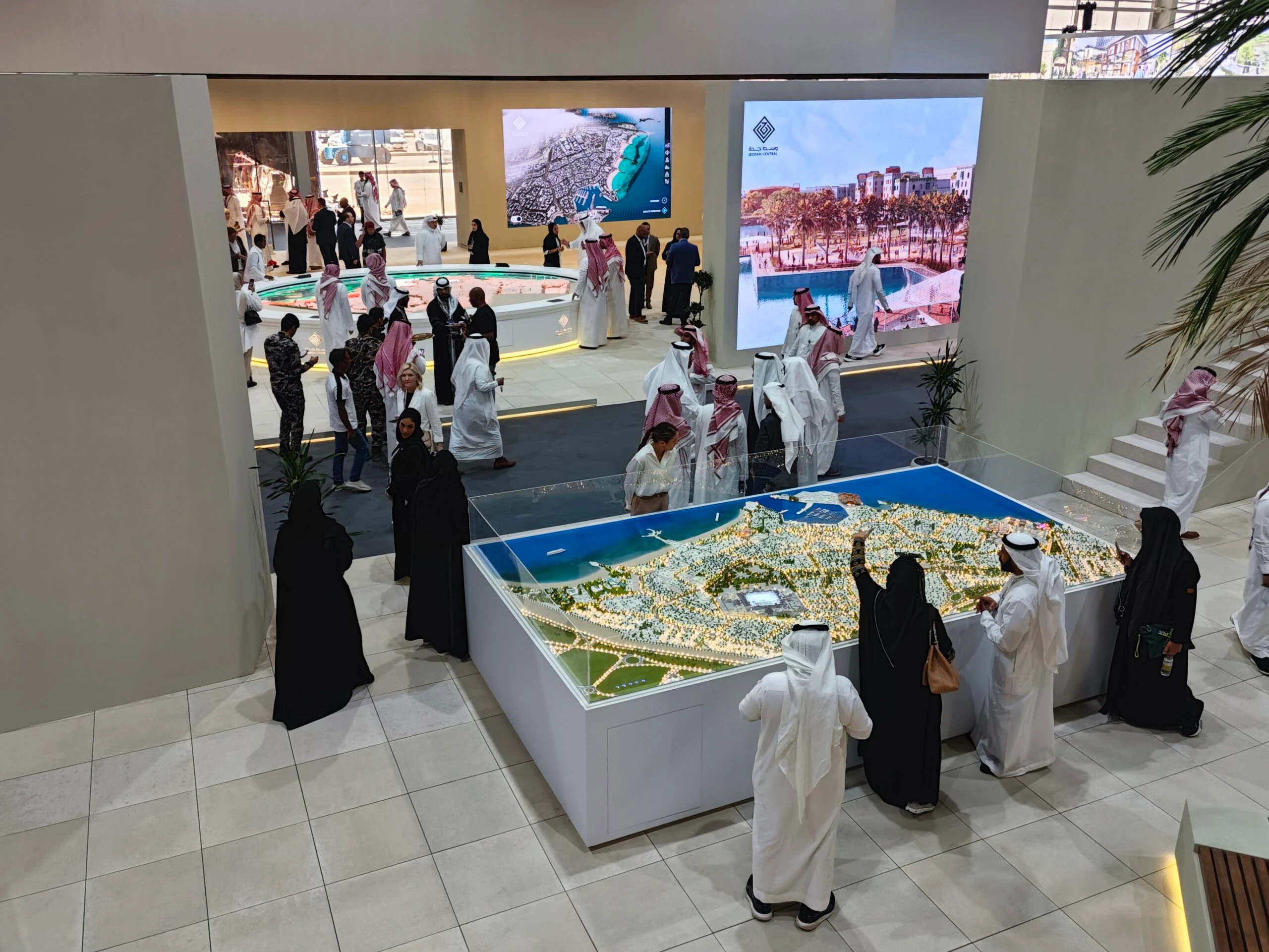 Visitors exploring an immersive digital twin model of Riyadh at Interactive Exhibition for Real Estate Developers, displayed on a large curved screen with a scale model in the foreground.