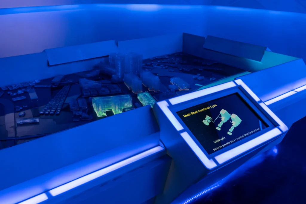 A futuristic interactive showroom featuring a digital touchscreen with digital twin and illuminated 3D city model, designed to guide visitors through an engaging customer journey. This setup exemplifies experiential marketing, combining real-time data, visual storytelling, and hands-on interaction to create a memorable and informative brand experience.