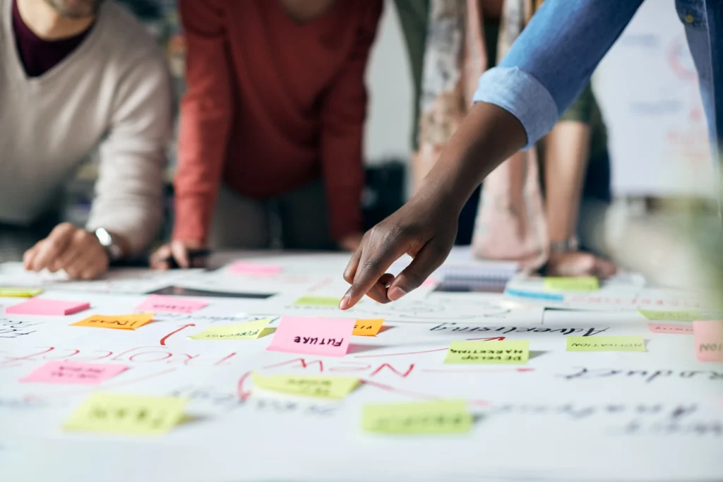 A close-up of a creative planning session, with team members collaborating over a table filled with colorful sticky notes labeled with terms like "future" and "innovation." The scene reflects the strategic mapping of the customer journey, essential for designing an interactive showroom and implementing effective experiential marketing strategies that engage audiences and drive meaningful brand interactions.