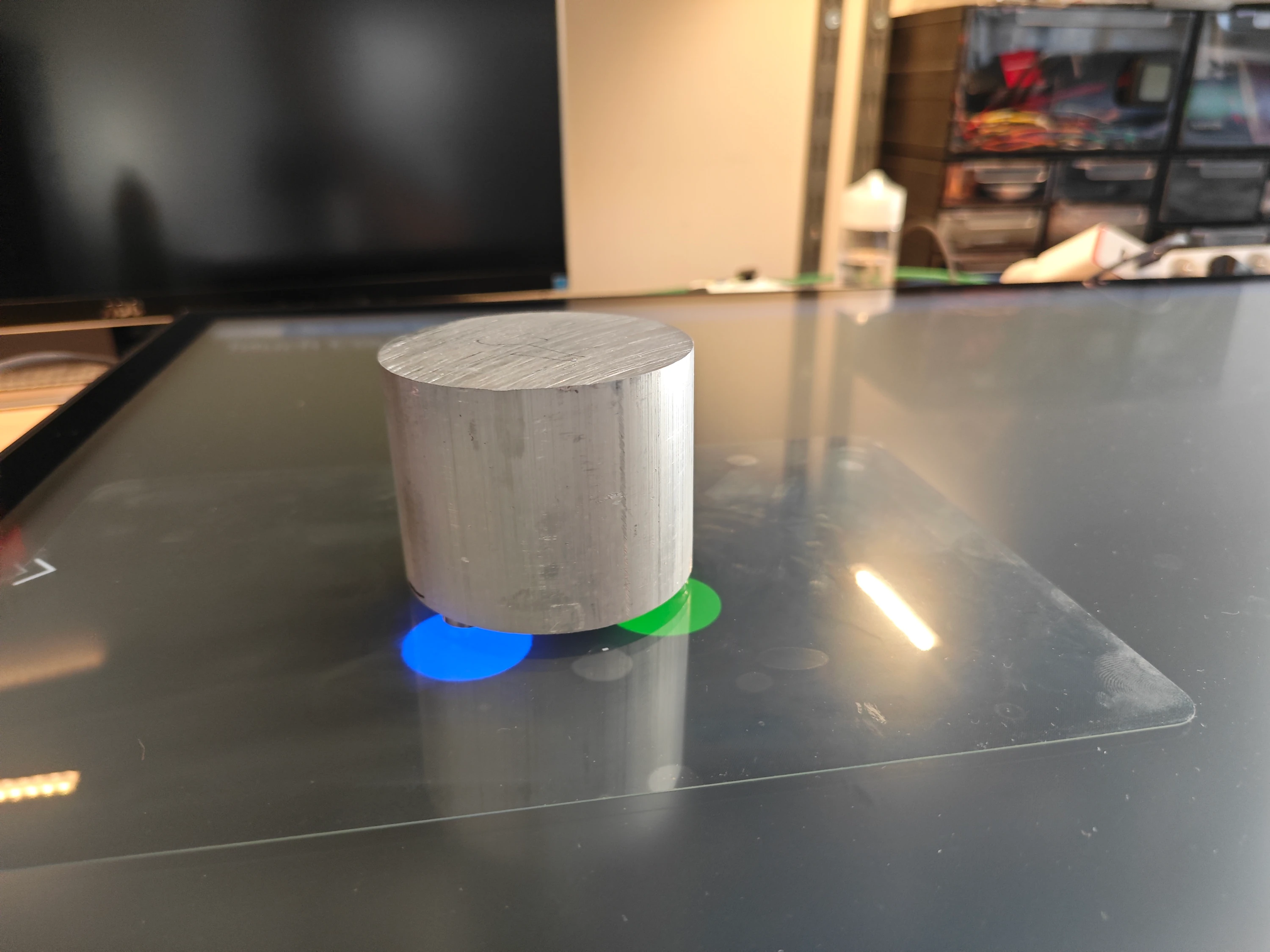 Rough-cut aluminium cylinder resting on a powered PCAP touch table; blue and green capacitive blobs glow beneath the raw token, illustrating early-stage object-recognition testing.