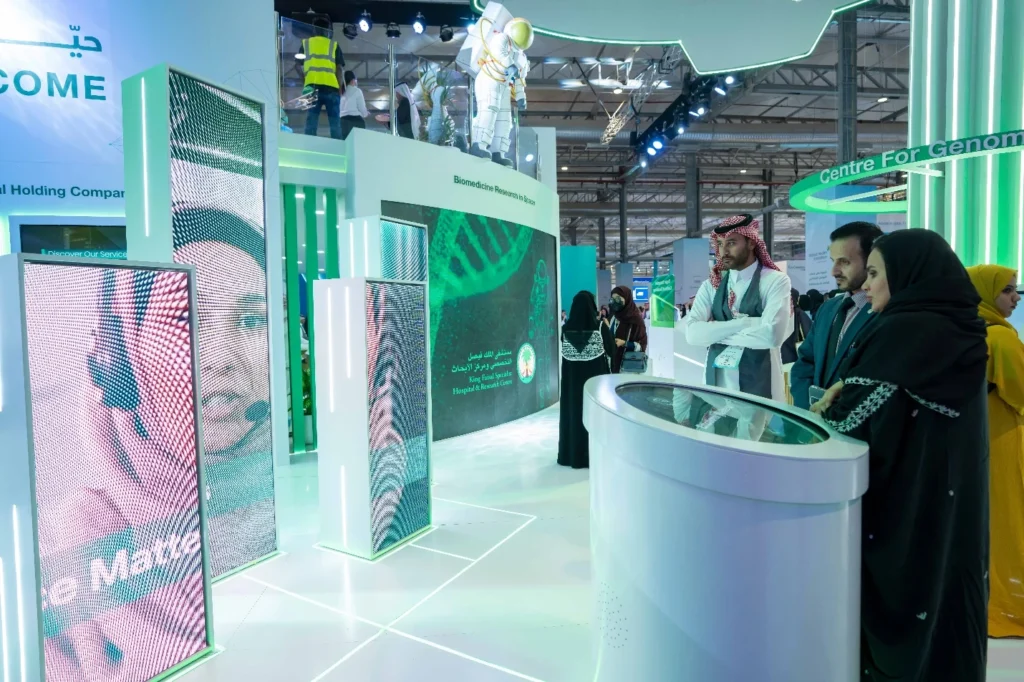 Interactive green LED booth at Global Health Exhibition in Riyadh, with visitors exploring genomics research displays and touchscreens.