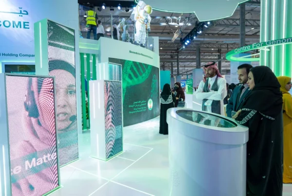 Interactive green LED booth at Global Health Exhibition in Riyadh, with visitors exploring genomics research displays and touchscreens.