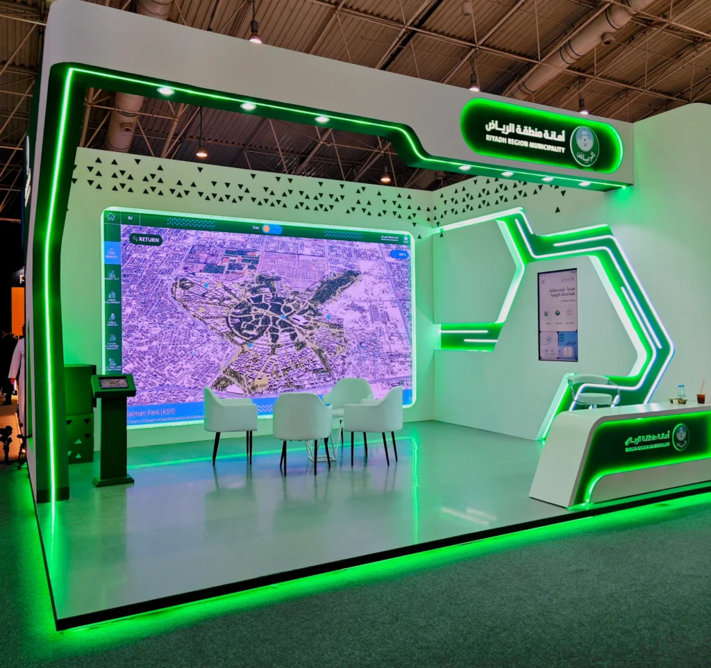 Close view of the Riyadh Digital Twin city map displayed on a big screen at FPF; Unreal Engine visualization framed by green LEDs with white meeting chairs.