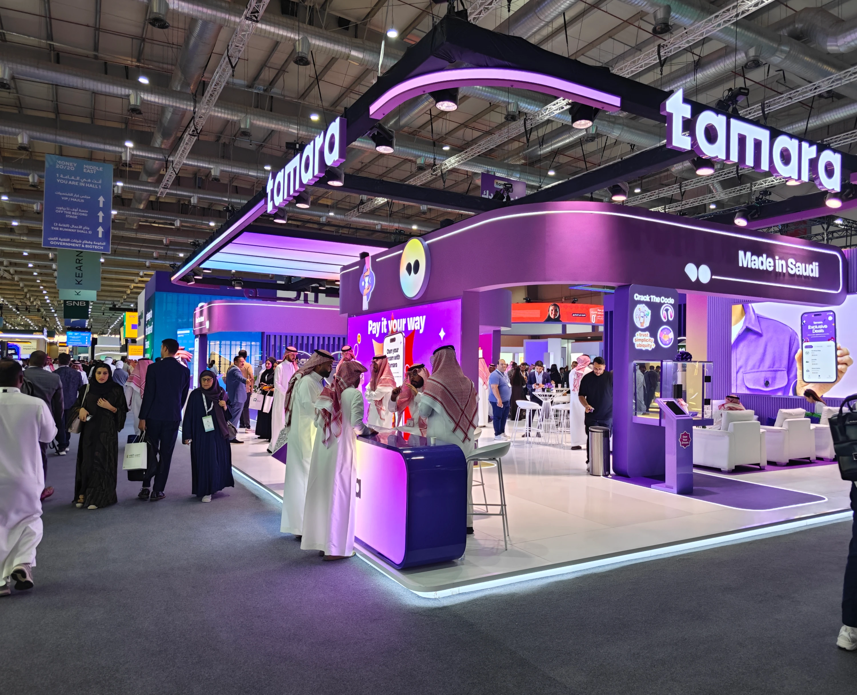 Tamara’s purple trade show booth at a Saudi fintech event with interactive counters, large digital displays and visitors exploring the stand.