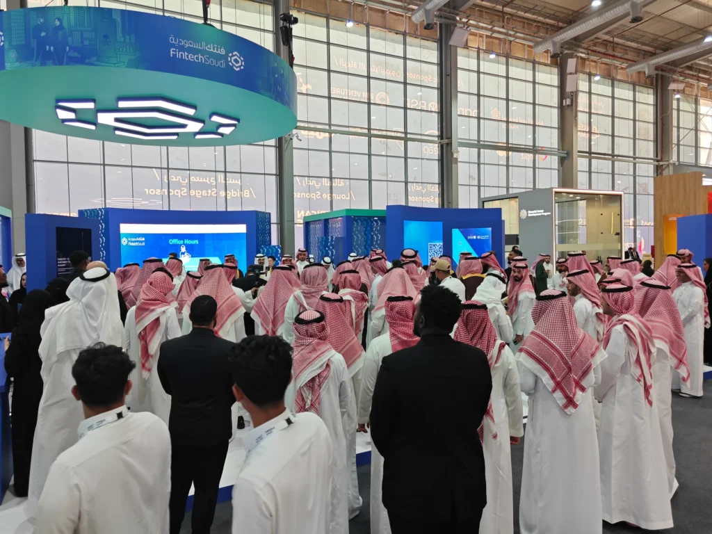 Crowd gathered at the Fintech Saudi stand during a live presentation, surrounded by digital screens and branding in a busy exhibition hall.