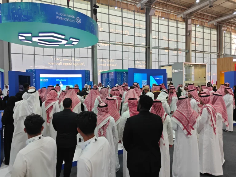 Original live-event photograph with large displays and interactive presentation stations.