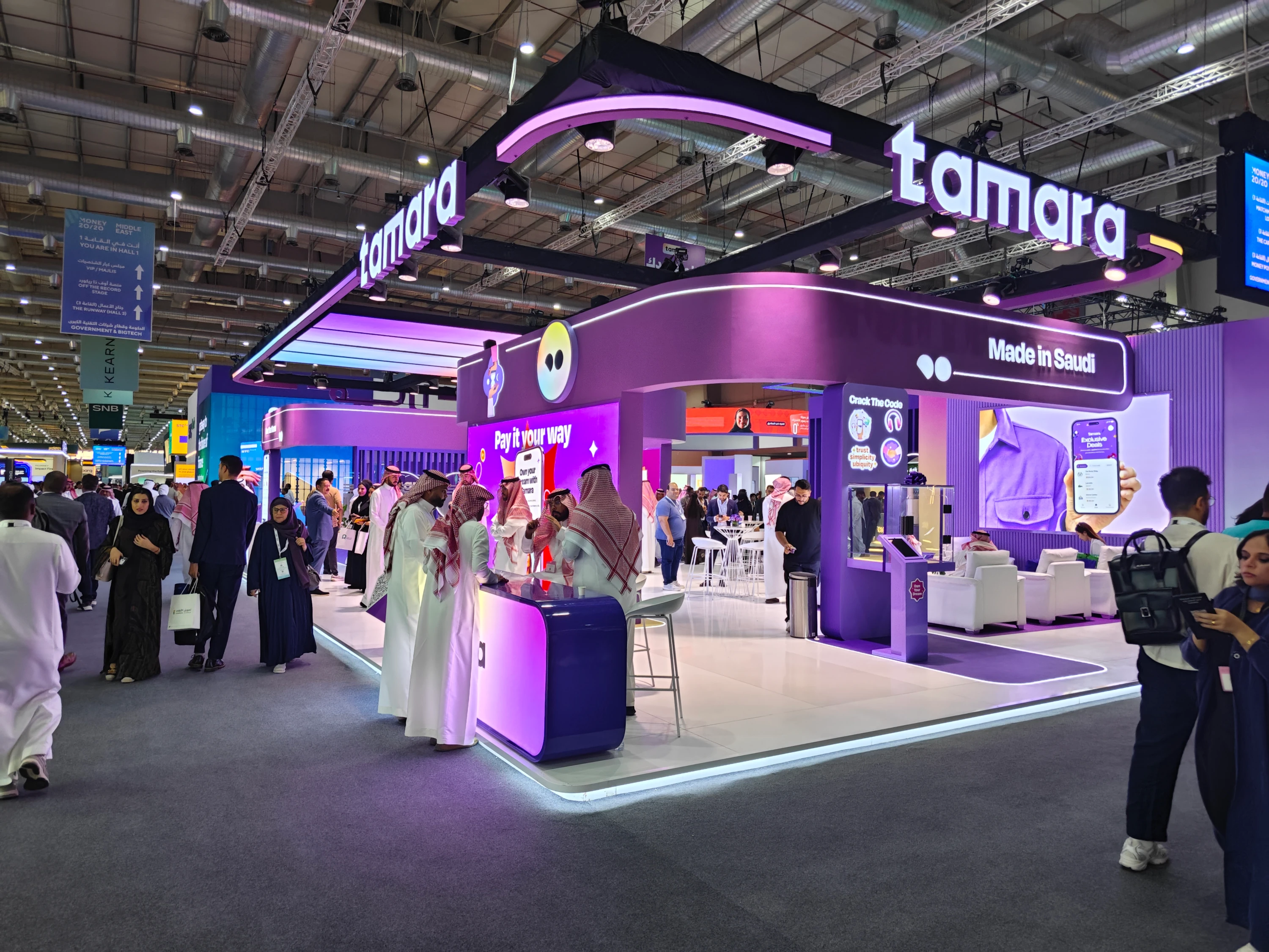 Crowded Tamara booth with bold purple branding, halo overhead sign, and LED content—designed for social visibility, fast engagement, and meeting-driven ROI.